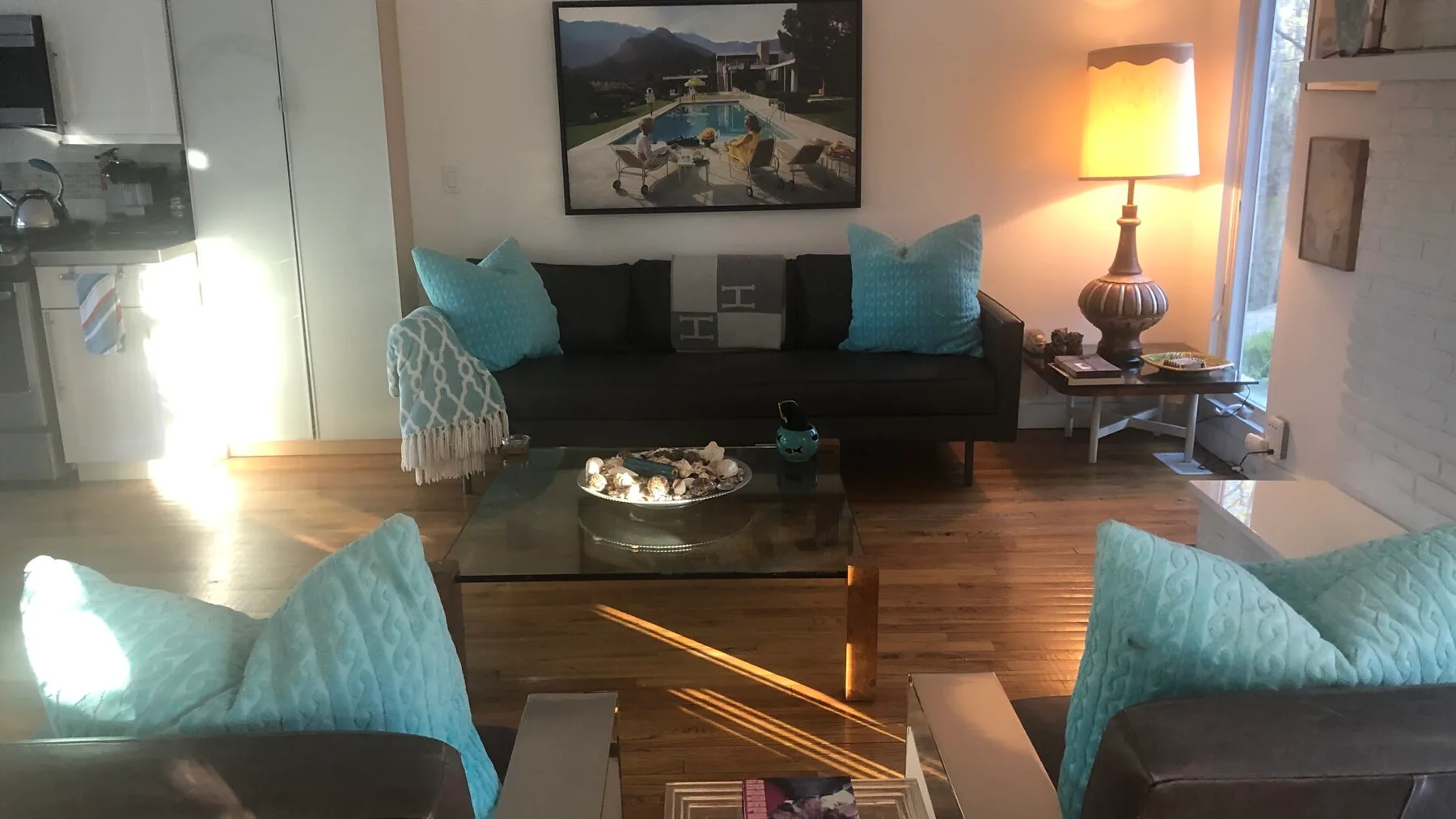Una sala de estar con asientos oscuros, cojines turquesa y una mesa de centro de vidrio.