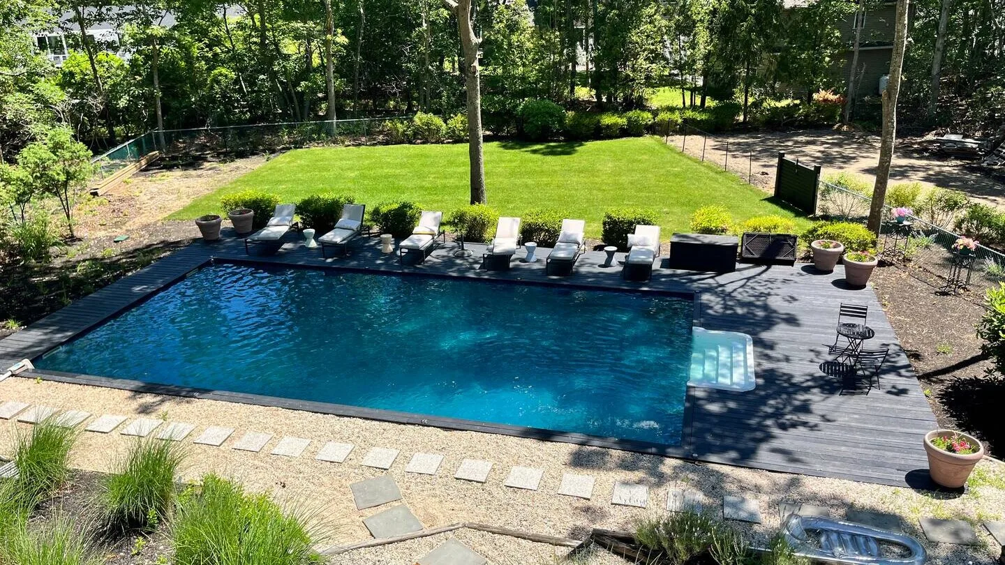 Una piscina en un patio está rodeada de asientos reclinables y césped verde.