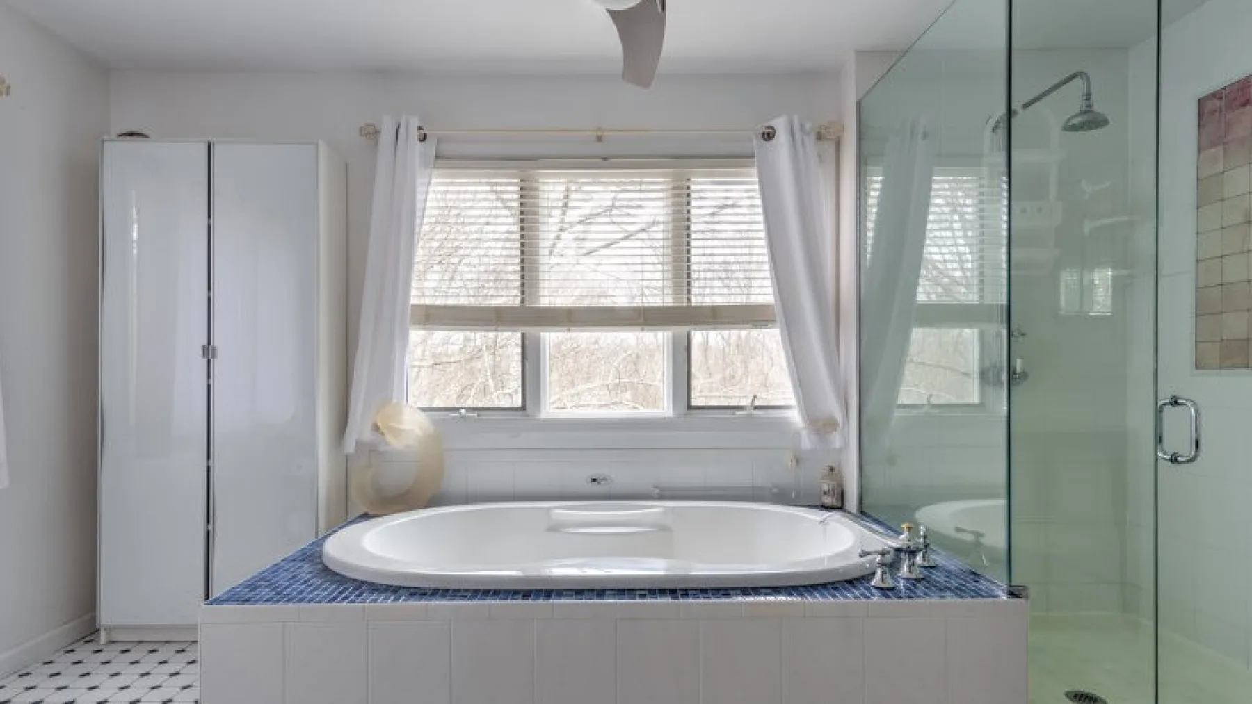 Un baño con una bañera bajo una ventana amplia y una ducha de vidrio.