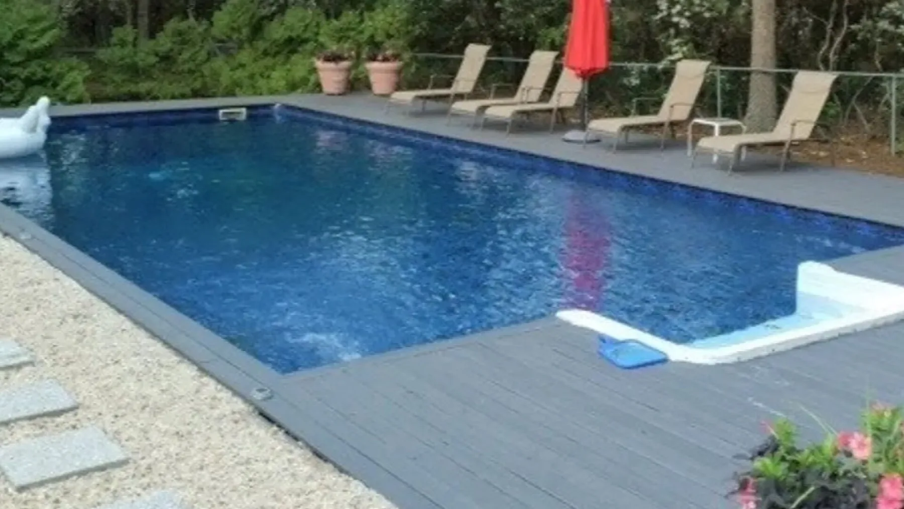 Una piscina al aire libre está rodeada por una terraza, tumbonas y vegetación.