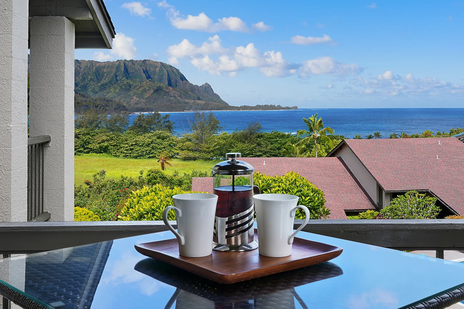 A tray with coffee cups sits on a table overlooking the ocean and mountains.