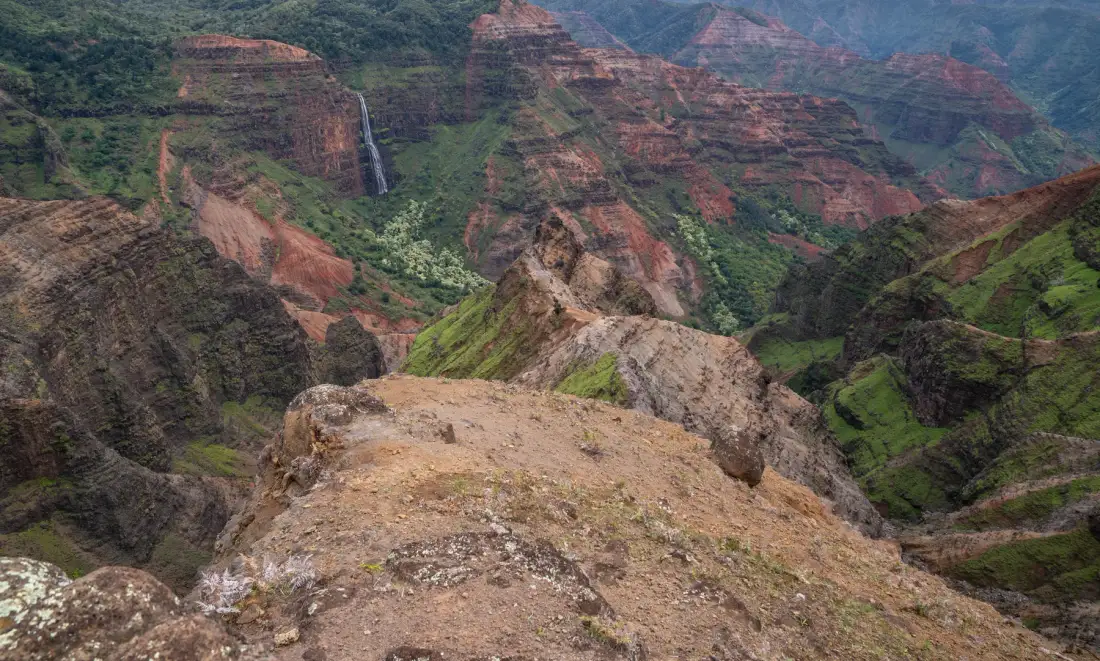 A rocky overlook opens onto a broad canyon with layered red cliffs.