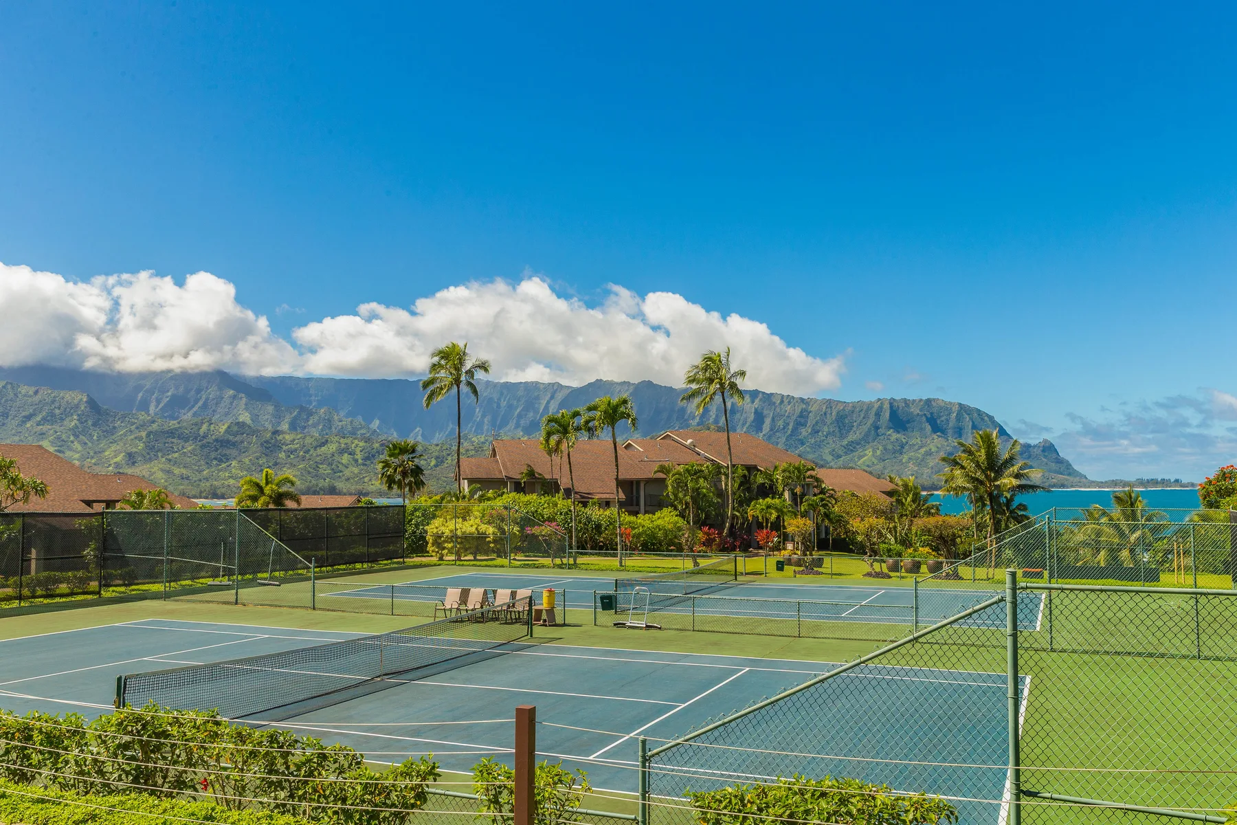 Outdoor tennis courts sit among tropical landscaping, with mountains and ocean in the background.