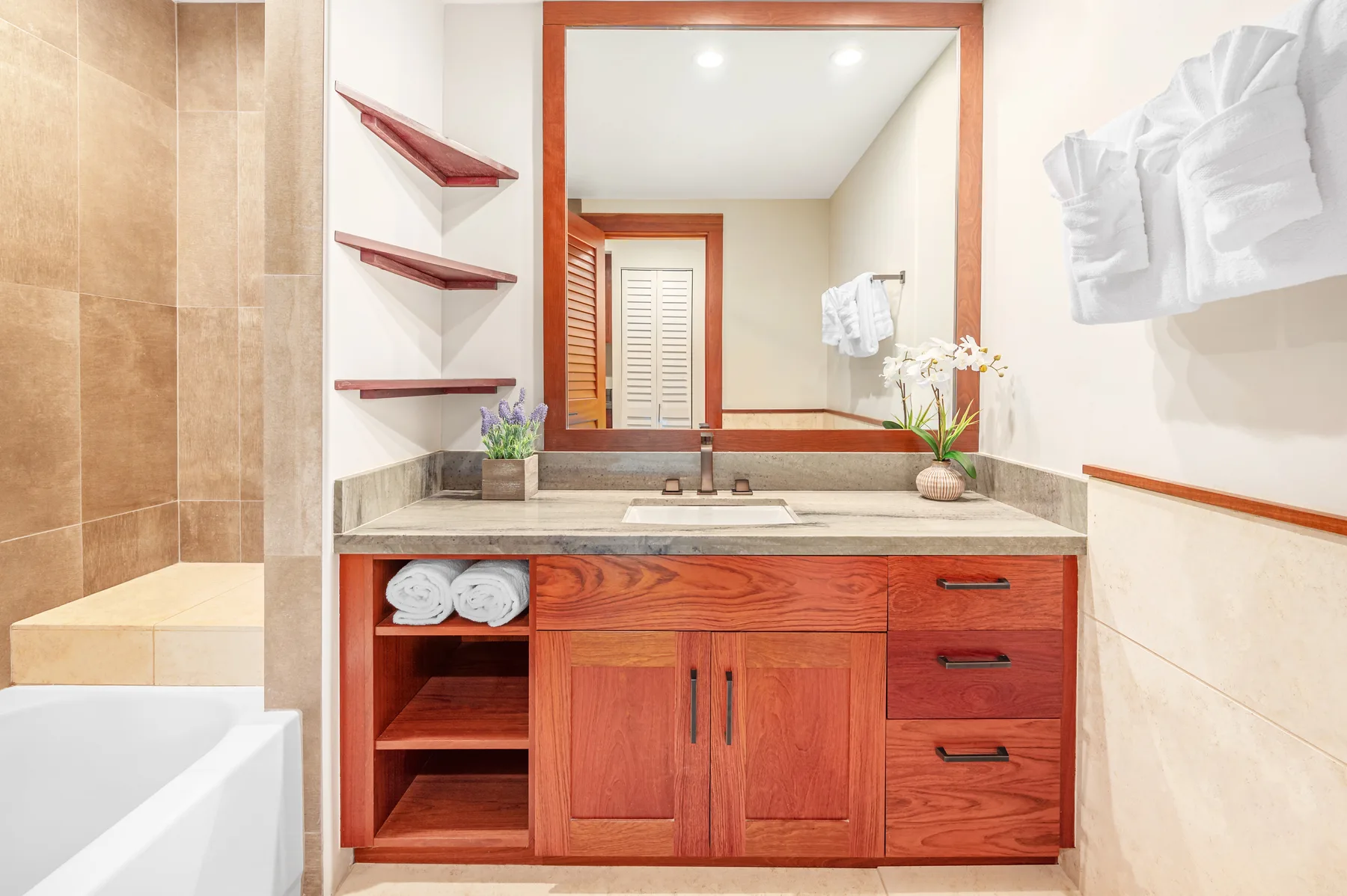 A bathroom vanity with a large mirror and a bathtub beside it.