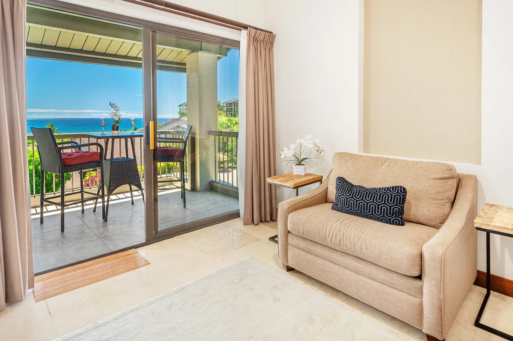 A living room with a beige sofa beside sliding glass doors opening onto a balcony.