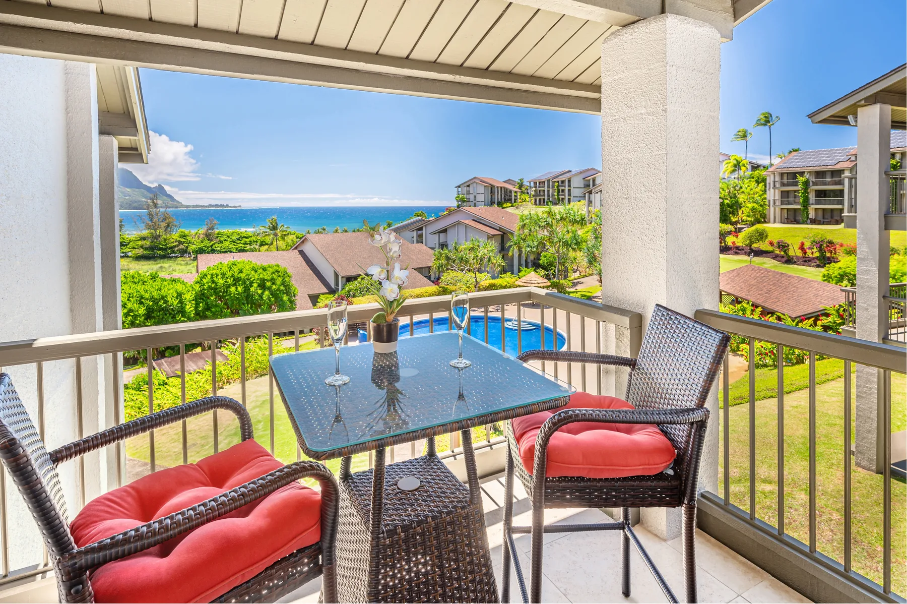 A covered balcony with patio seating overlooks landscaped grounds and the ocean.