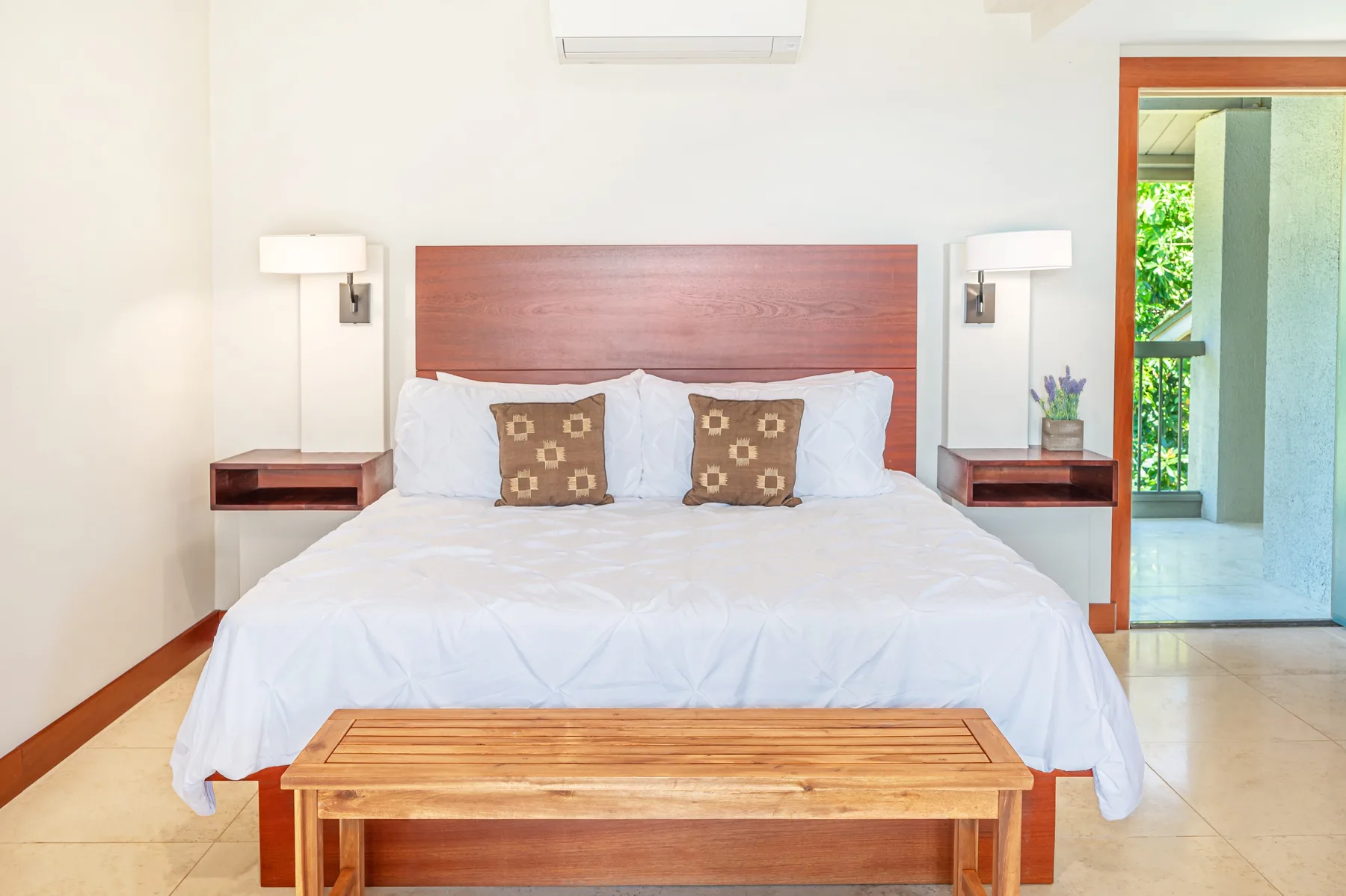 A bedroom with a neatly made bed and a wooden bench at its foot.