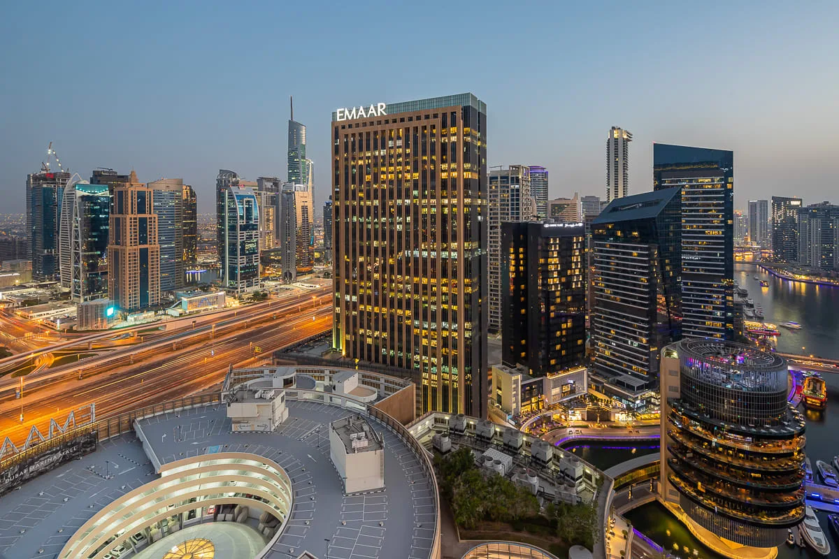 A city skyline at dusk with illuminated high-rise buildings and busy roads.