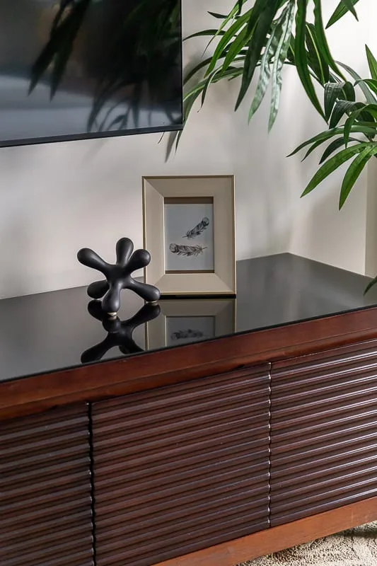A living room console displays framed art and a small sculpture beneath a wall-mounted screen.