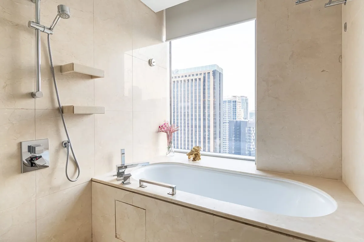 A bathroom with a large bathtub beside a wide window overlooking city buildings.