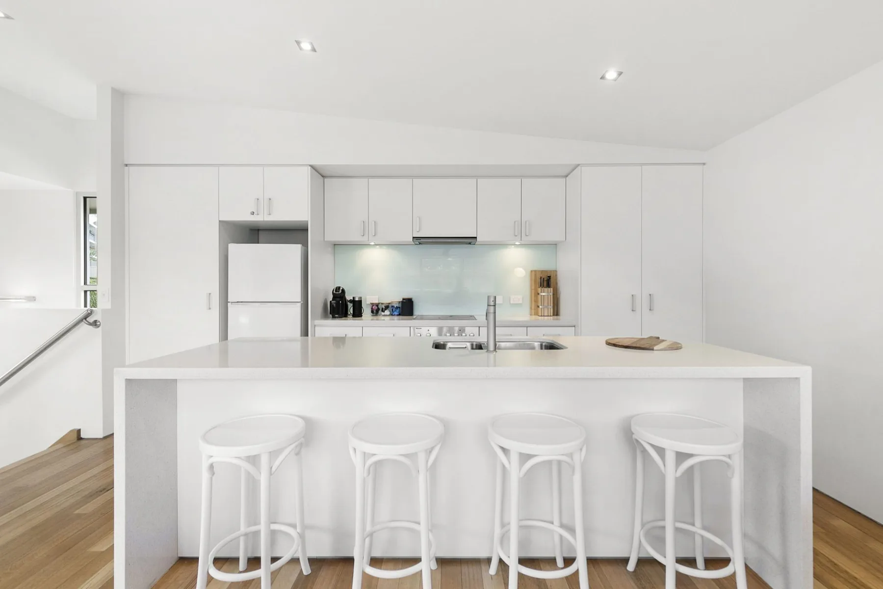Una cocina blanca y luminosa con una isla larga y taburetes.