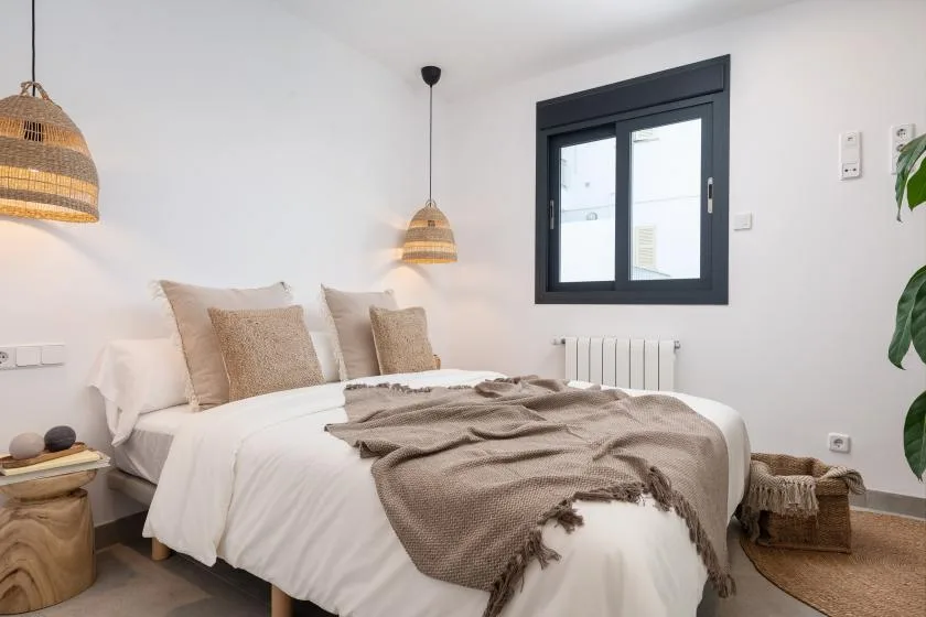 Un dormitorio con una cama bien tendida y una ventana de marco oscuro.