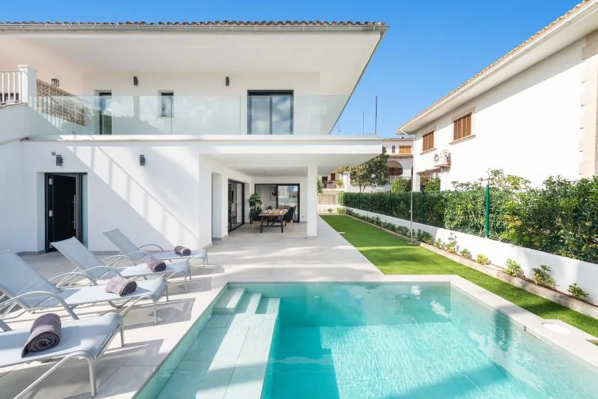 A modern white house opens onto a swimming pool and paved patio.
