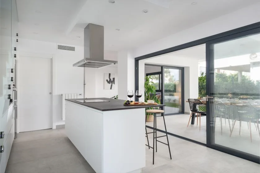 Una cocina moderna se abre a un comedor a través de grandes puertas de vidrio.