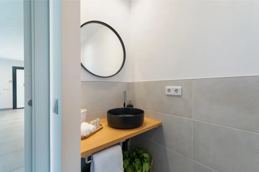 Un lavabo de baño con una pila negra, un espejo redondo y paredes revestidas de azulejos.