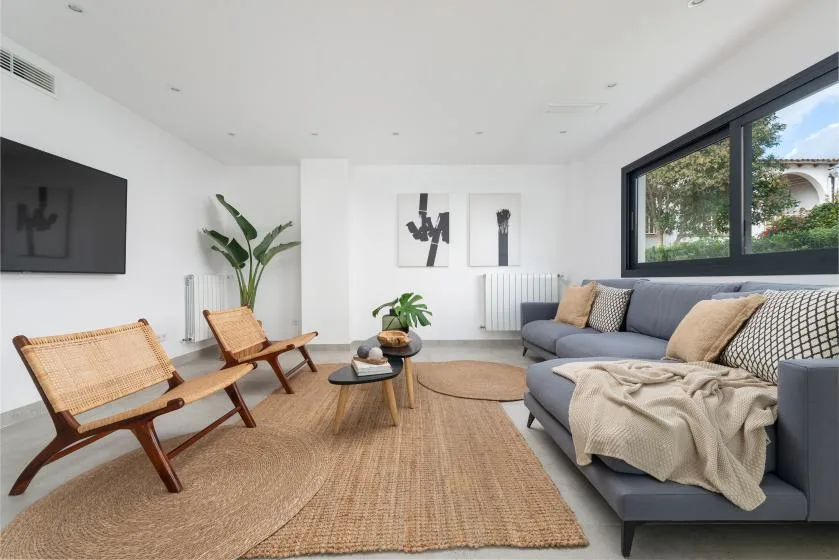 Una sala luminosa con un sofá gris, sillas tejidas y una alfombra grande.