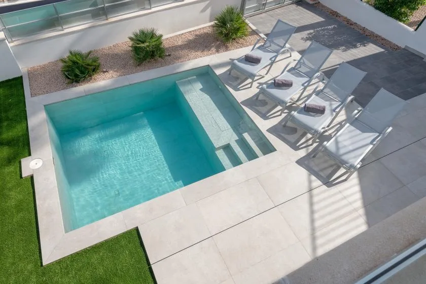 Una piscina exterior con escalones está rodeada de zonas pavimentadas para sentarse.