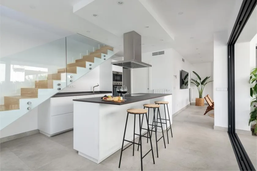 Una cocina moderna y luminosa con una isla central y una escalera con barandilla de vidrio.
