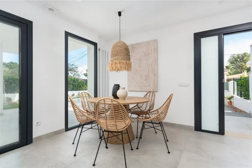 Comedor con asientos tejidos alrededor de una mesa de madera y una lámpara colgante.