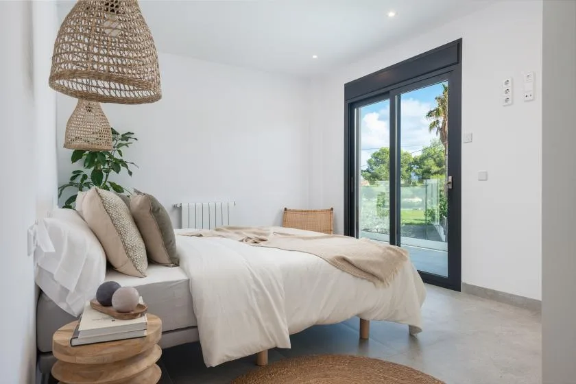 Un dormitorio luminoso con una cama tendida junto a una gran puerta de vidrio.