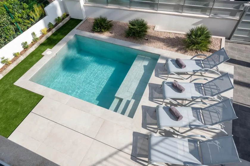 Una piscina exterior está junto a un patio pavimentado con asientos reclinables.