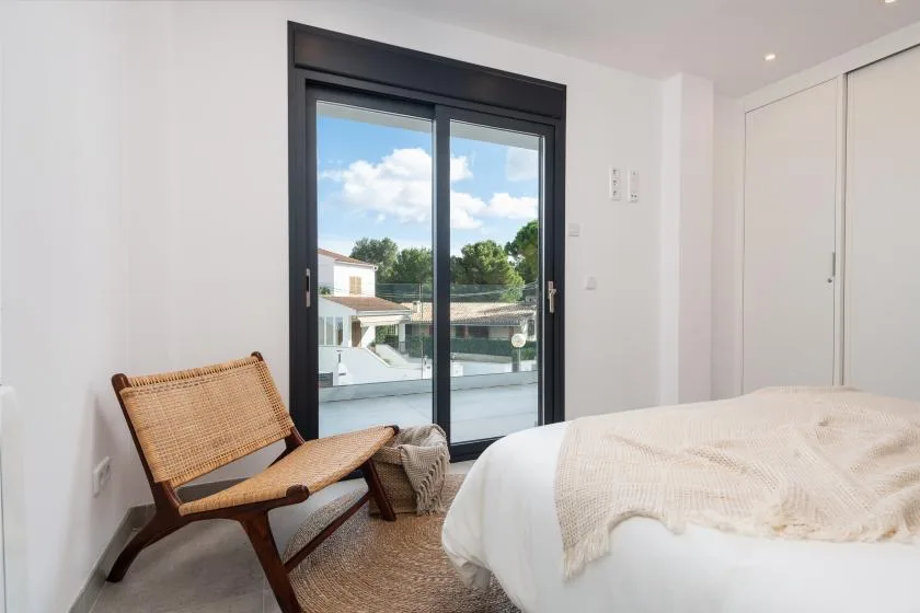Un dormitorio luminoso con una cama, asiento tejido y una gran puerta de vidrio.