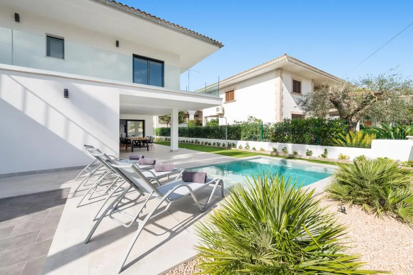 A modern house opens onto a swimming pool, with lounge seating and garden plants.