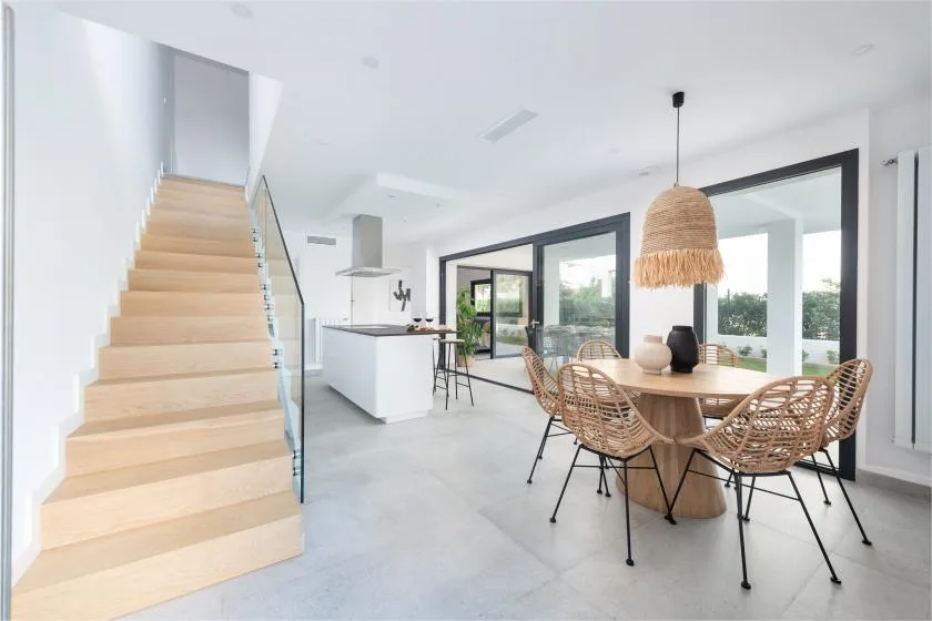 Un comedor y cocina de planta abierta, luminosos, con una escalera y asientos tejidos.
