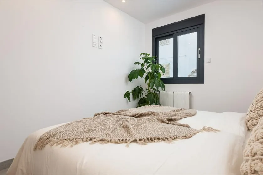 Un dormitorio con una cama cubierta por una manta tejida y una planta junto a la ventana.