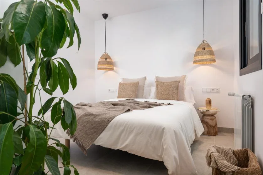 Un dormitorio con una cama, lámparas colgantes tejidas y una planta frondosa.
