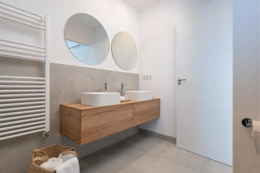 Un baño moderno con lavabo doble y espejos redondos.