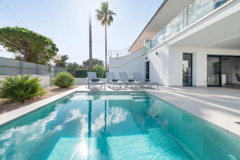 Una piscina al aire libre junto a un edificio blanco moderno y asientos en el patio.