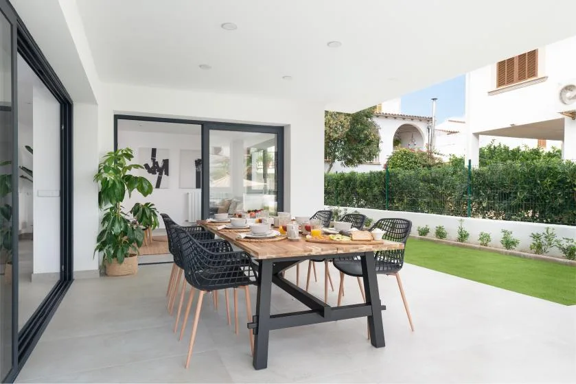 Un comedor al aire libre con una mesa larga y sillas junto a un césped verde.