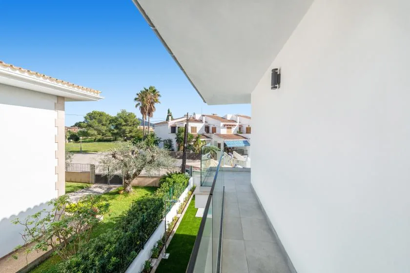 Un balcón cubierto da a un jardín ajardinado y casas cercanas.