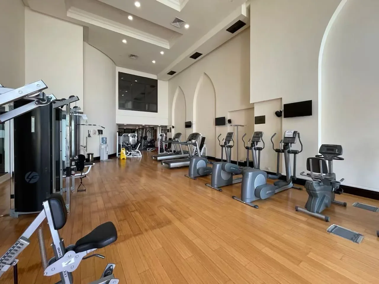 Un gimnasio amplio con máquinas de ejercicio distribuidas sobre un suelo de madera.