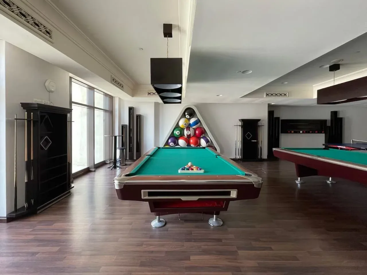 Una sala de billar con una mesa de paño verde y bolas de colores en un extremo.