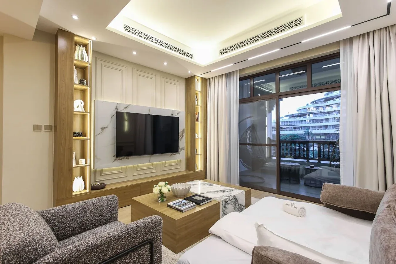Una sala luminosa tiene asientos, un televisor y grandes ventanales con vista a un balcón.