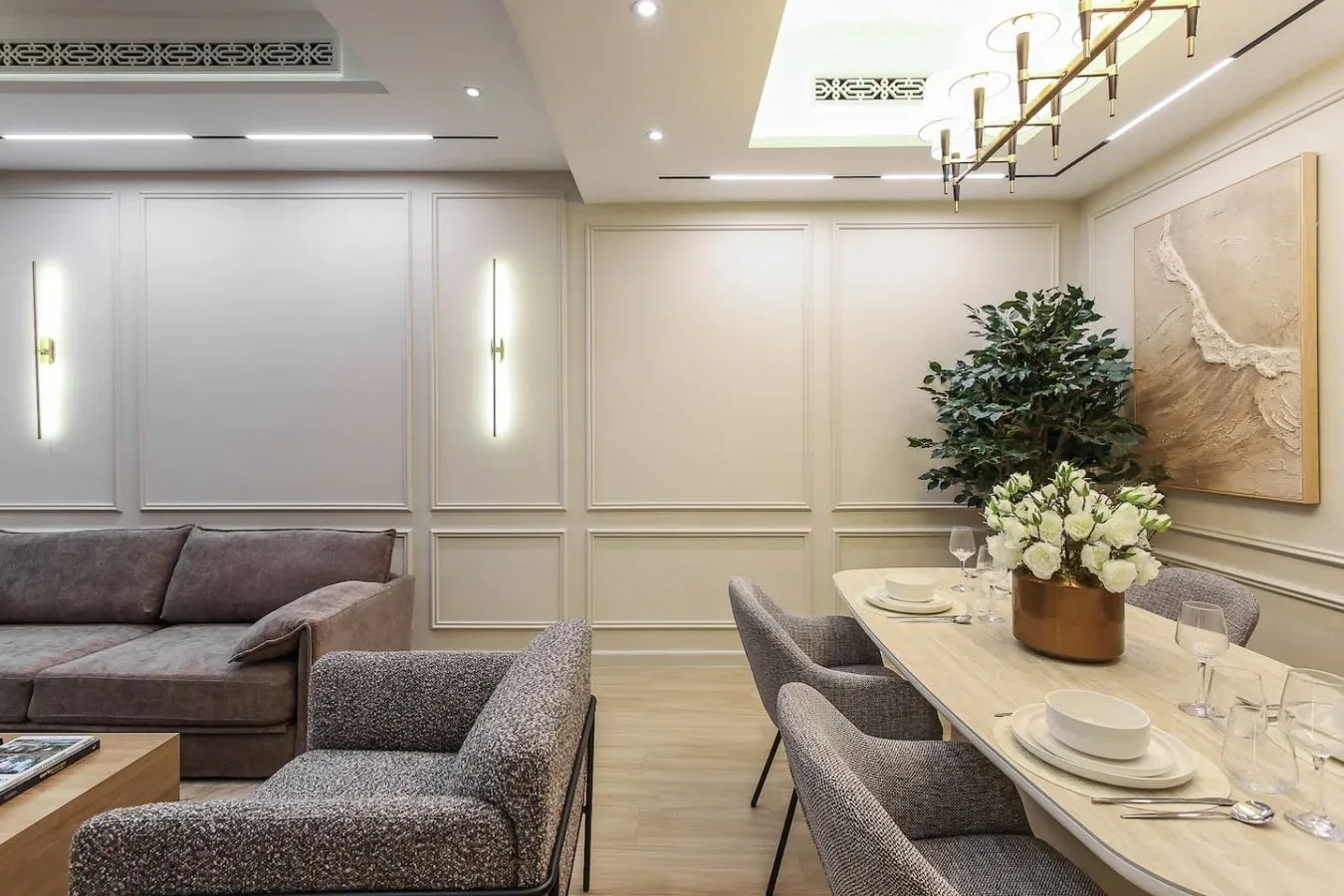 Un comedor con la mesa puesta junto a una zona de estar y una planta en maceta.