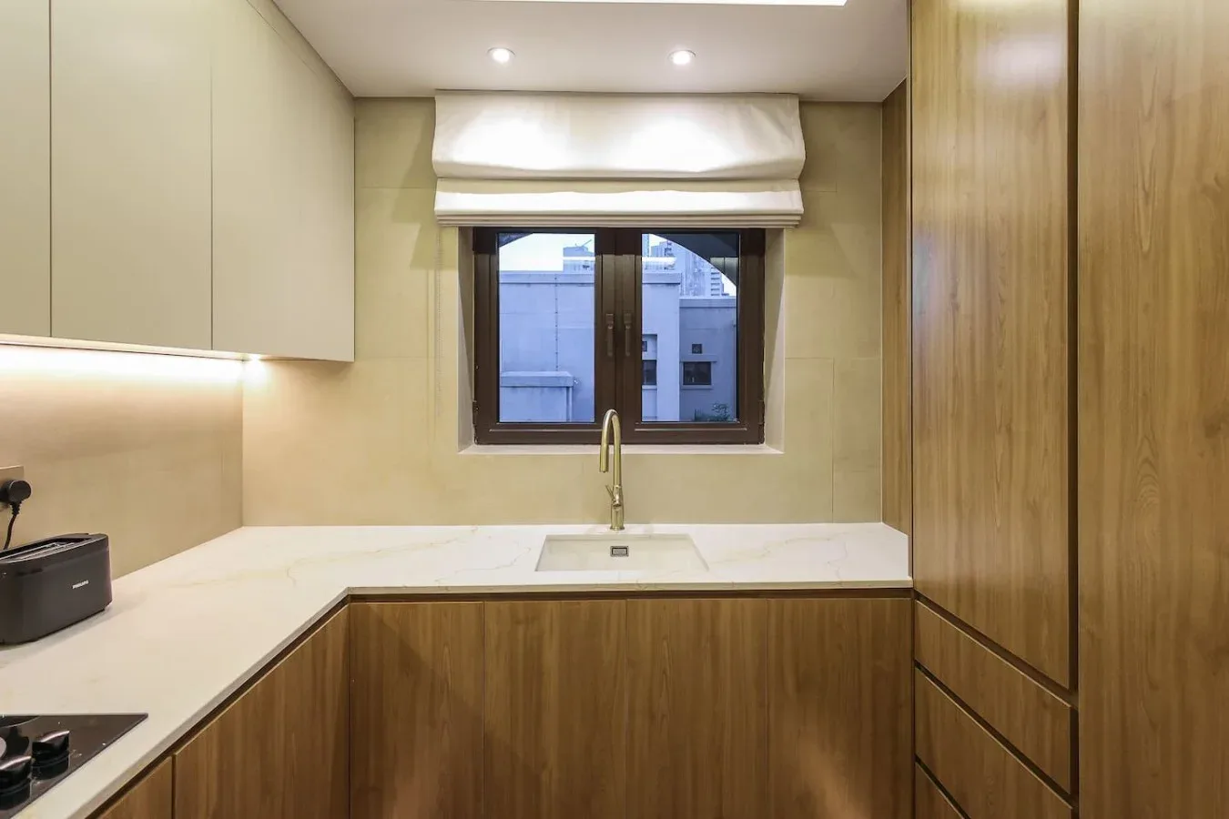 Una cocina compacta con encimeras claras, gabinetes de madera y una ventana sobre el fregadero.
