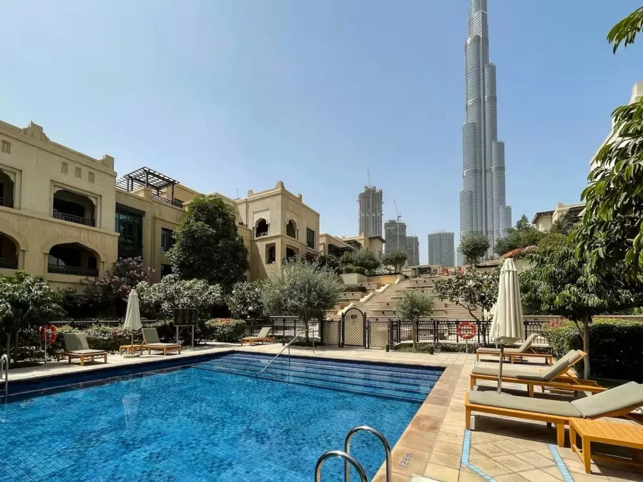 Un patio soleado con piscina, asientos de descanso y un alto horizonte urbano al fondo.