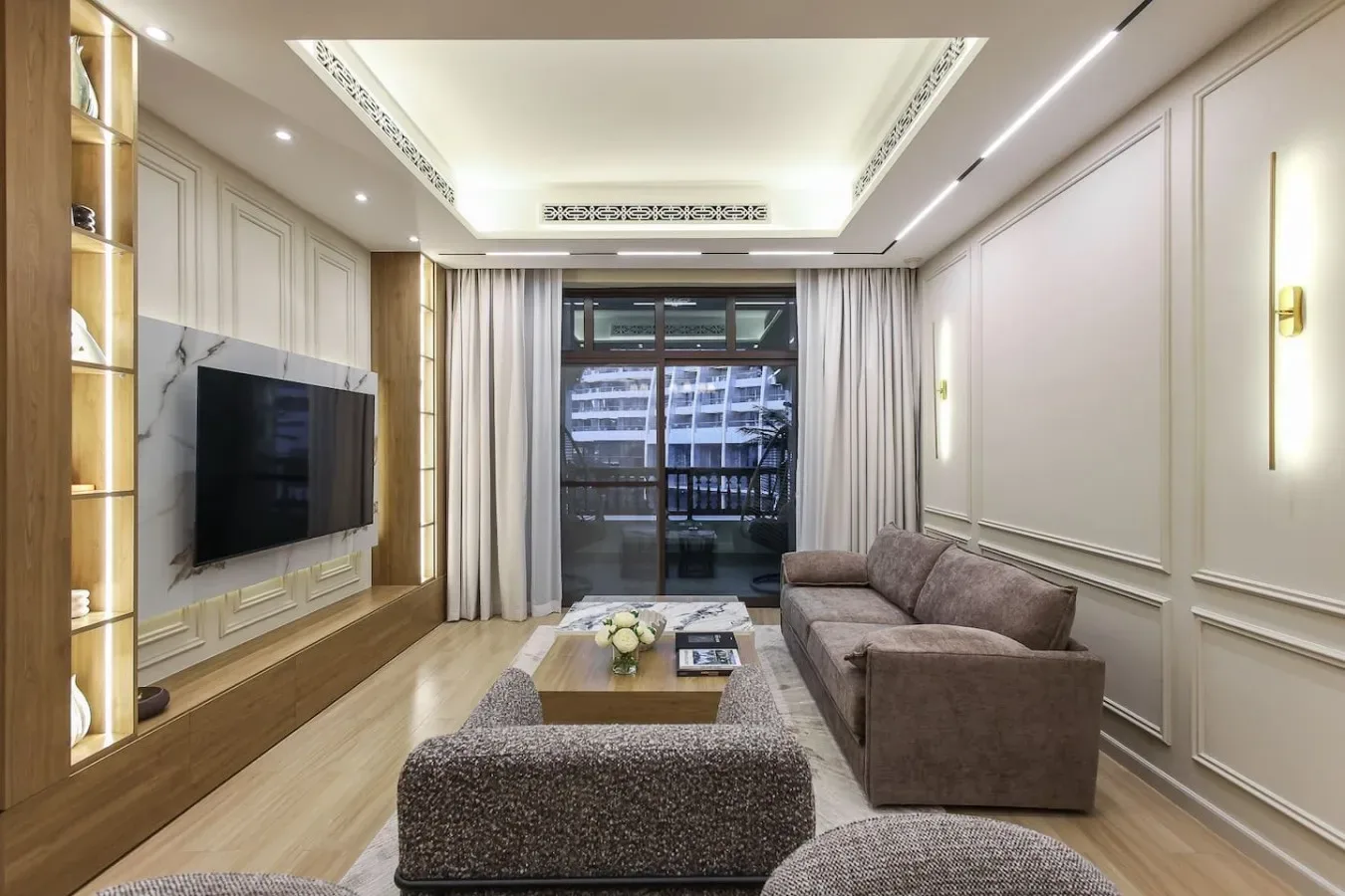 Una sala de estar con asientos, un televisor y ventanas con vista a edificios cercanos.