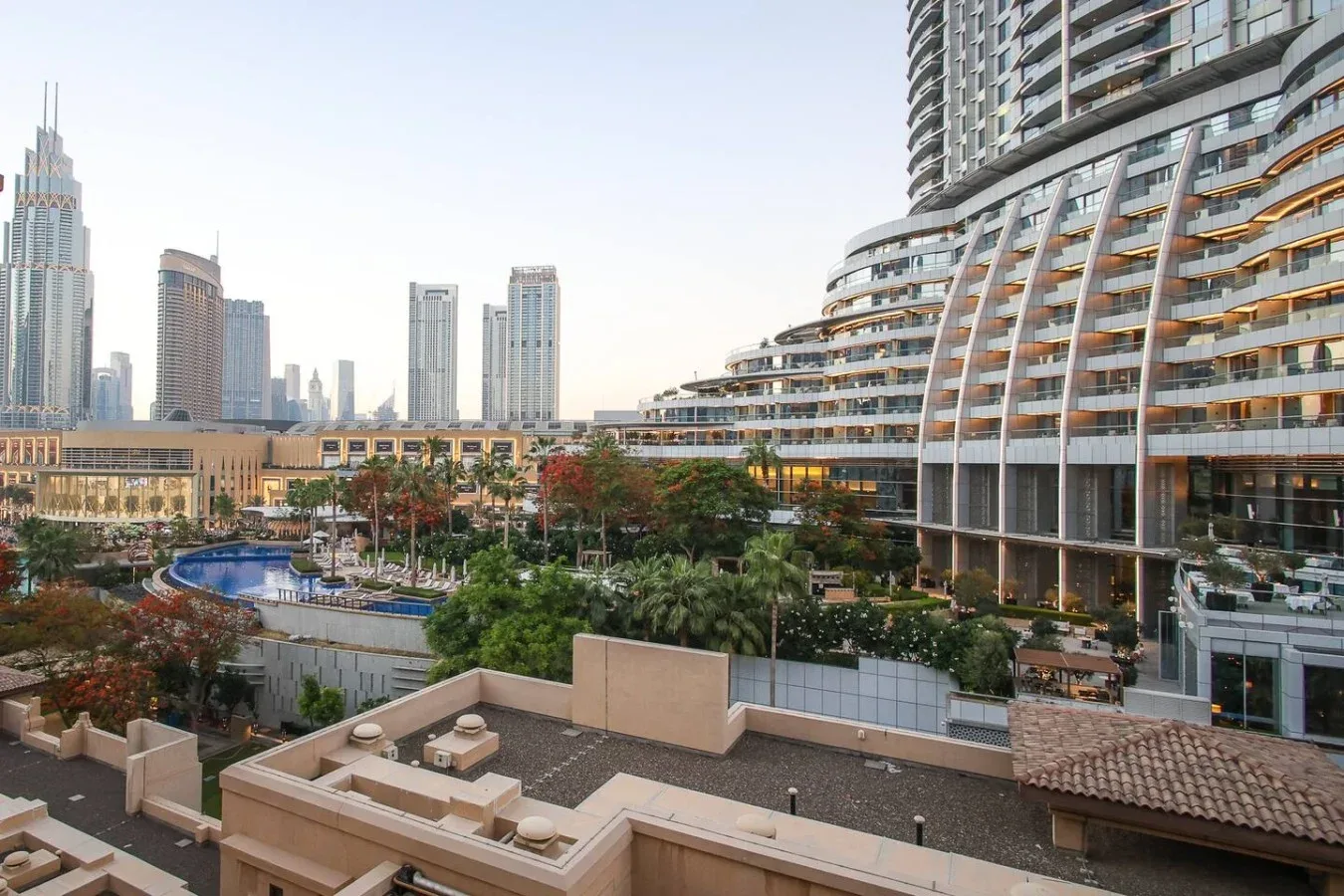 Una vista urbana con un edificio alto curvo que domina jardines y una piscina.