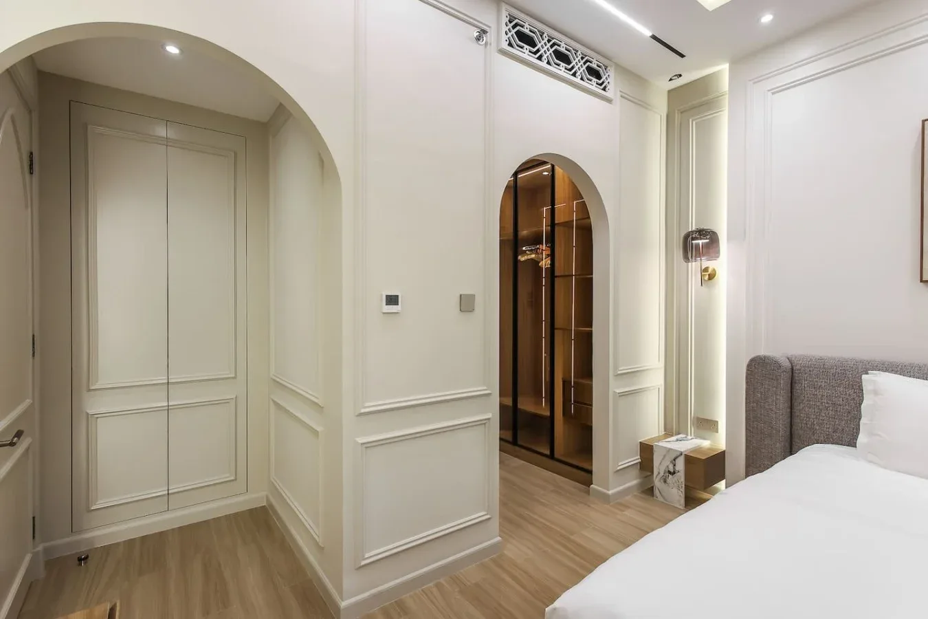 Un dormitorio luminoso con una cama junto a una entrada arqueada y estantes empotrados.