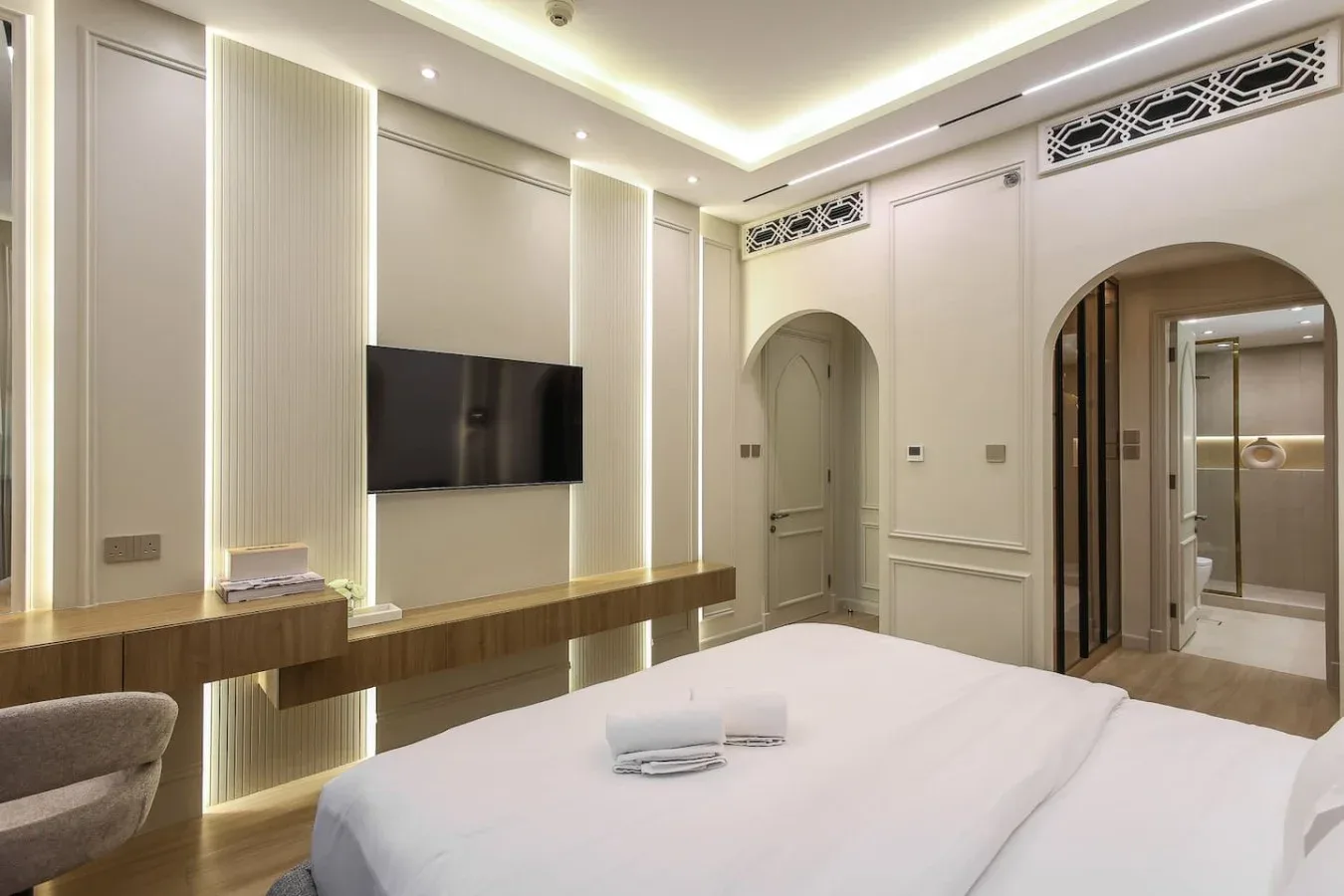 Un dormitorio con una cama, un televisor en la pared y entradas arqueadas.