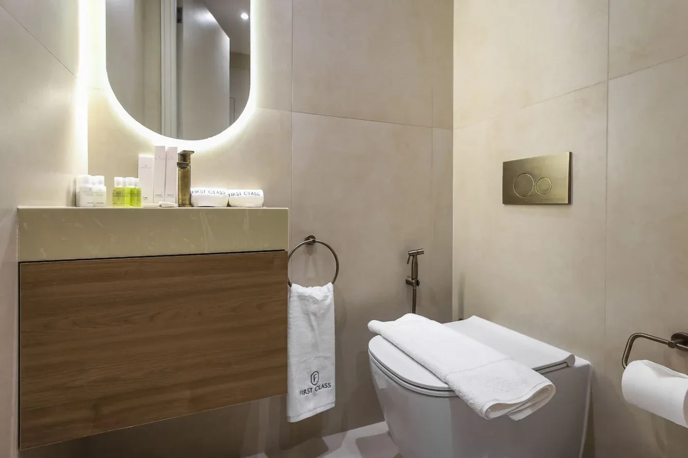 Un baño con inodoro, un mueble con frente de madera y un espejo redondo iluminado.