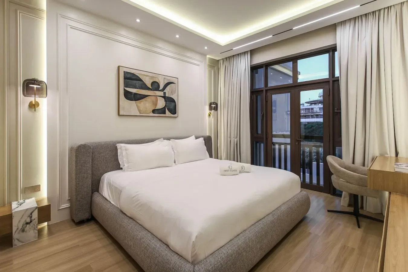 Un dormitorio con una cama bien arreglada junto a una ventana amplia con cortinas.