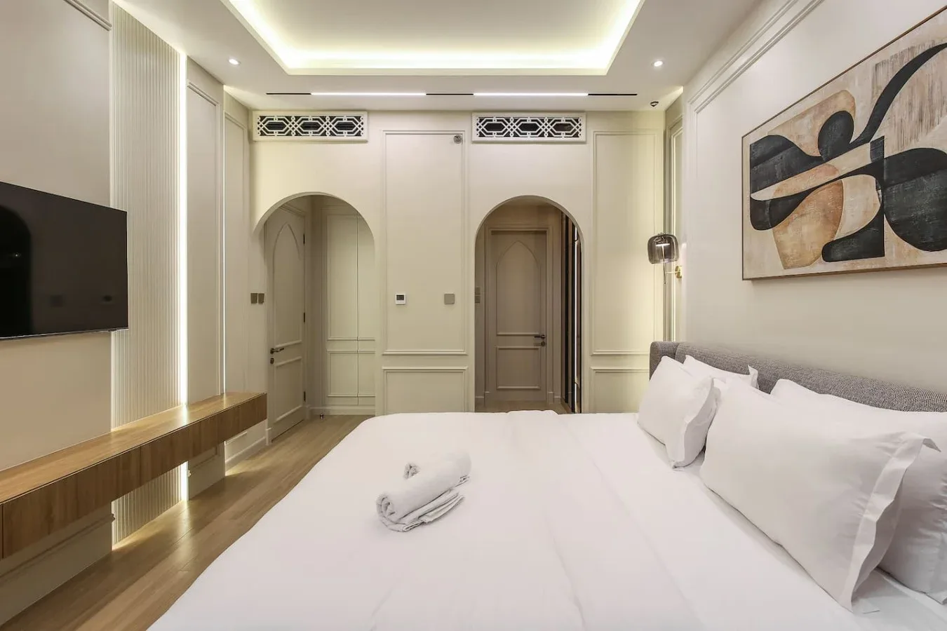 Dormitorio con una cama grande, televisor de pared y una obra abstracta.