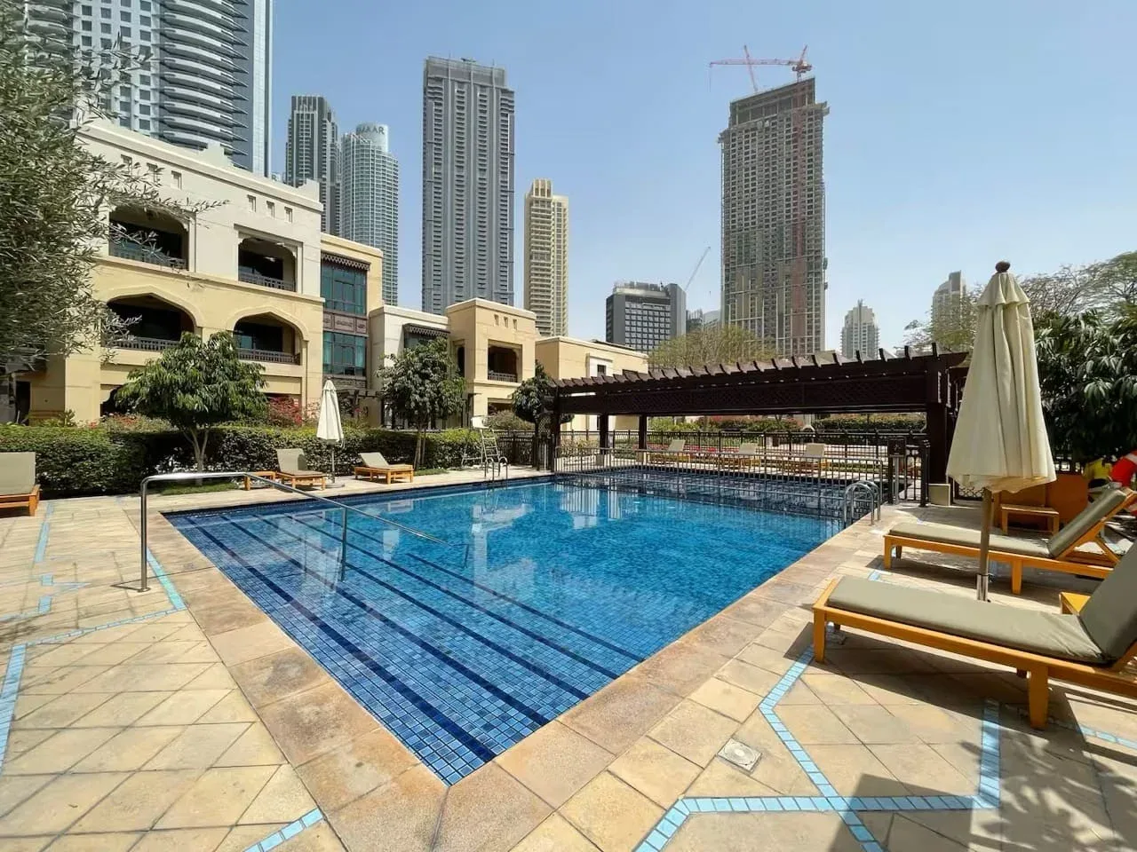 Una piscina al aire libre con tumbonas y edificios altos de la ciudad al fondo.