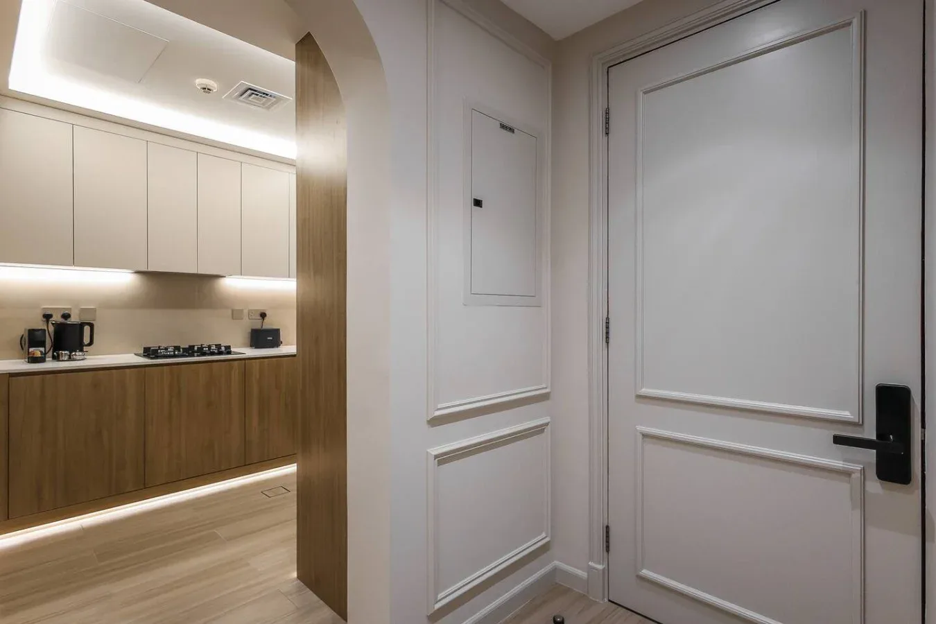 Una cocina con gabinetes claros y una isla en tono madera, vista a través de un arco.