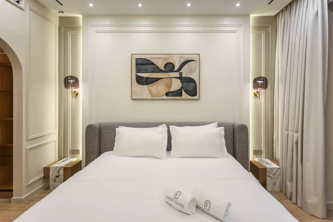 Un dormitorio con una cama tendida, una obra enmarcada y cortinas.